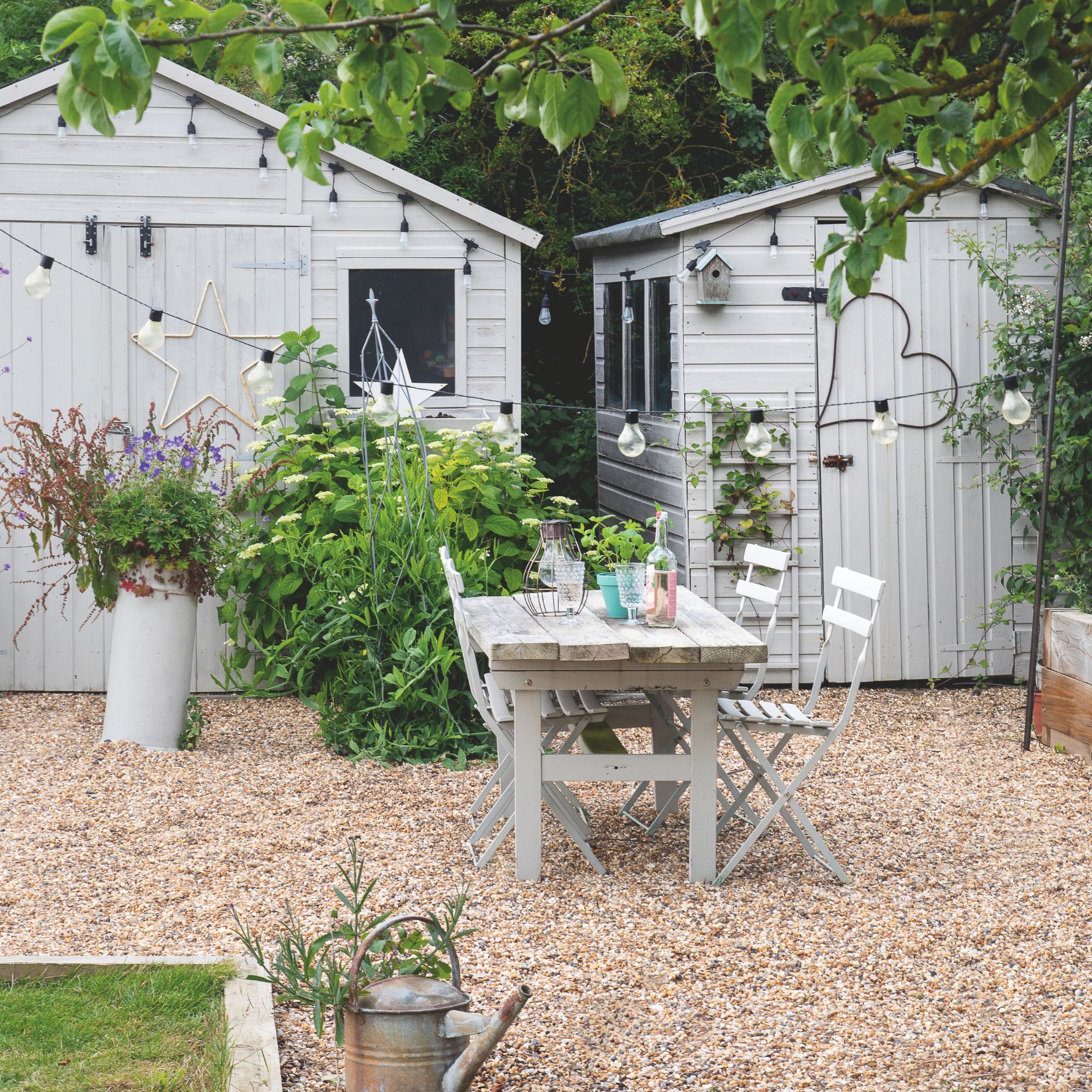 Gravel garden with a wooden dining set and two grey sheds behind it