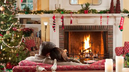 A man and woman sitting of sofa in front of lit fire at Christmas
