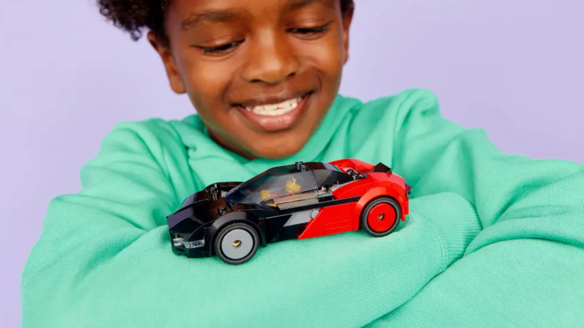A child smiles with the Lego EV Supercar set on their folded arms