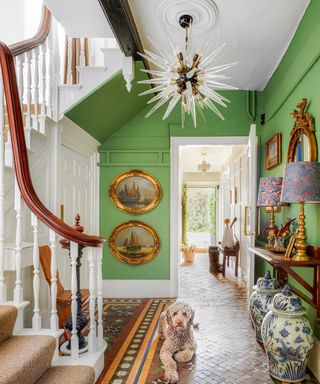 Traditional green period hallway with brass framed wall art, ornamental pots, mirror, tiled flooring and dog