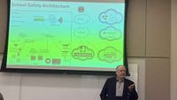 A professor discusses school safety systems in front of a screen.
