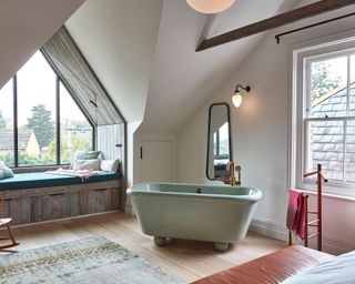 Loft bedroom with vanity under eaves and freestanding green bath