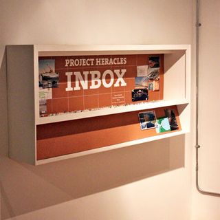 A cork-board ’Inbox’, accompanied by thumb tacks, invites visitors to pin up any new postcard entries here.