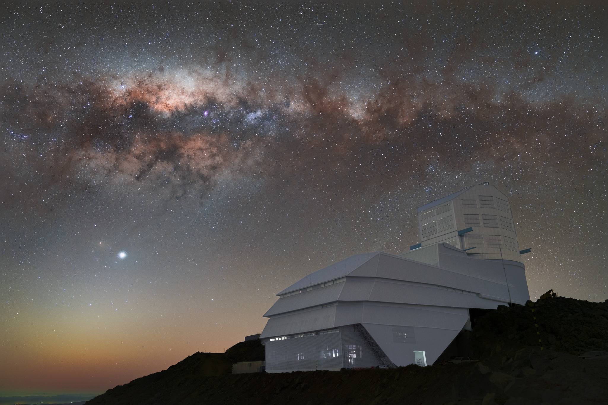 سلسلة من السحب الحمراء والأرجوانية فوق مبنى أبيض يقع على منحدر