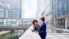 Two business people having a conversation outside in front of modern glass buildings