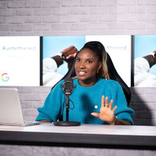 Denise Lewis in a studio wearing a blue jumper, presenting her podcast