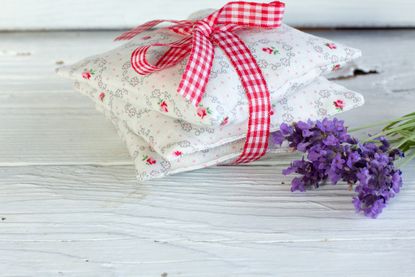 Lavender pillows tied in a bow with a red and white gingham ribbon on the table next to some dried lavender