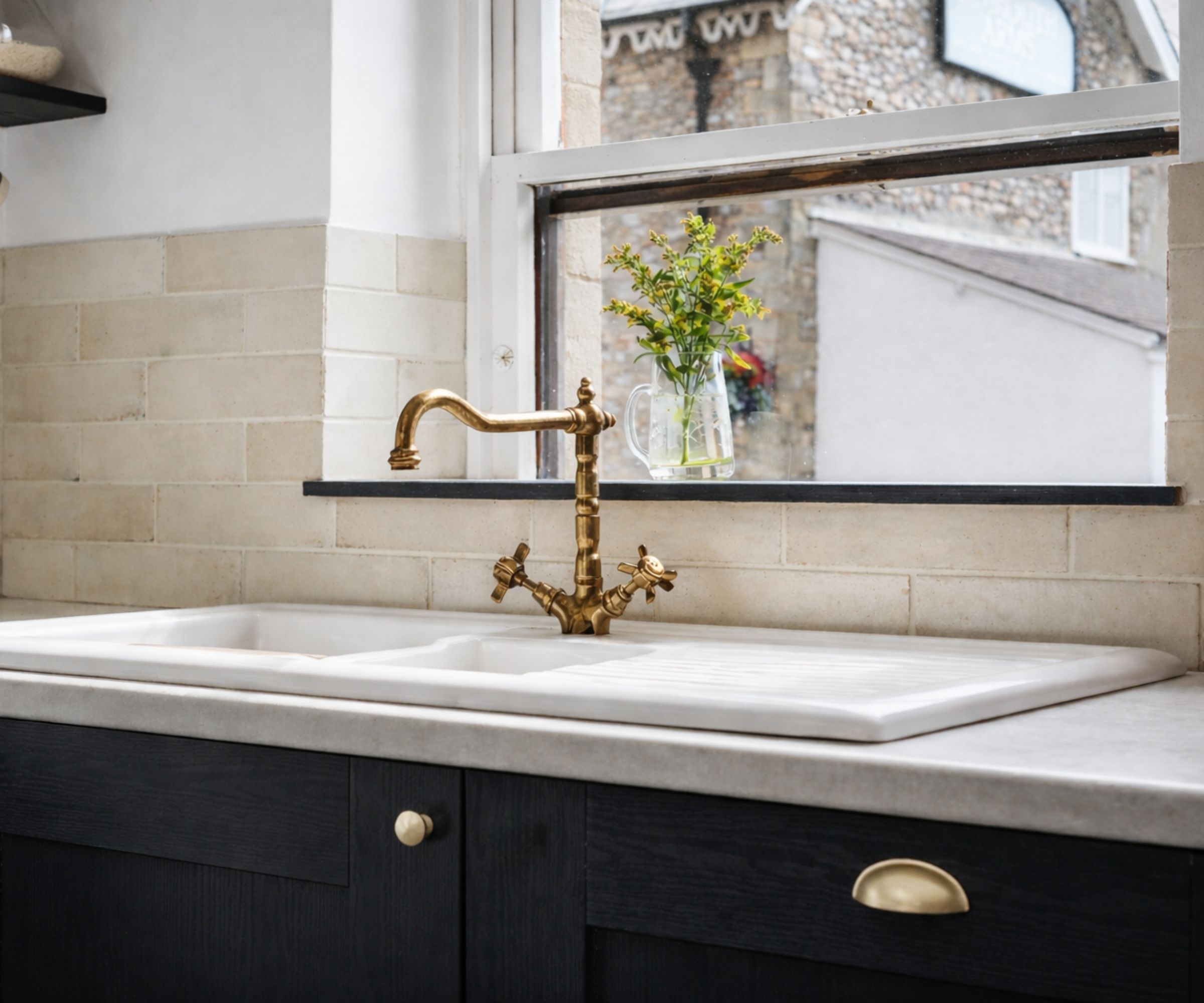 A farmhouse sink with a tall brass faucet and a beige tiled splashback