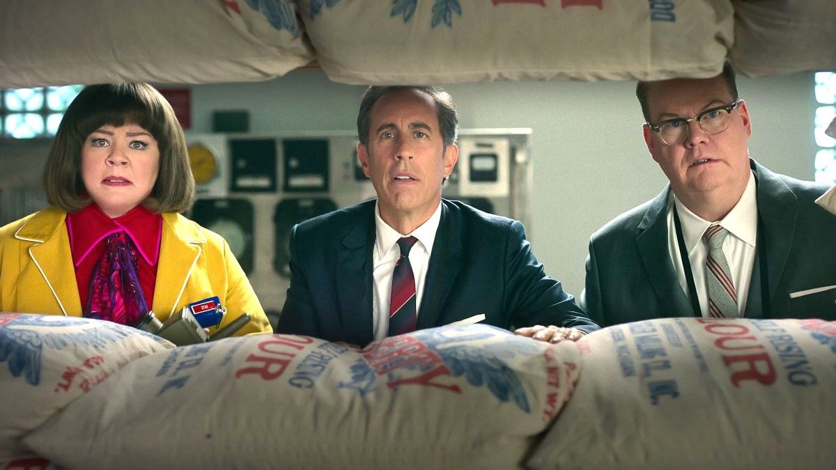 Melissa McCarthy as Donna Stankowski, Jerry Seinfeld as Bob Cabana and Jim Gaffigan as Edsel Kellogg III hide behind bags of flour in the Netflix movie Unfrosted.