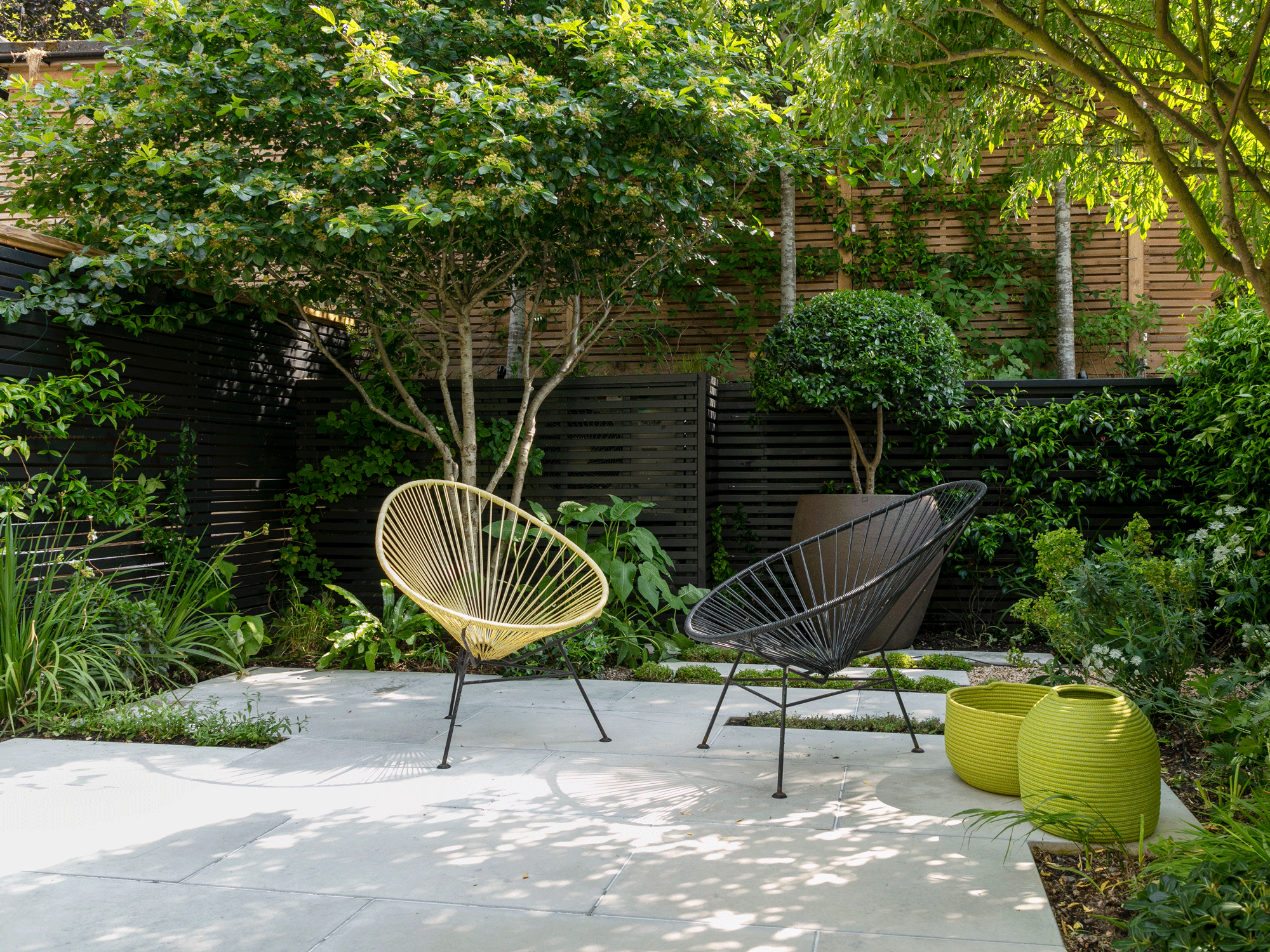 small patio with paving, planting including trees, and garden chairs