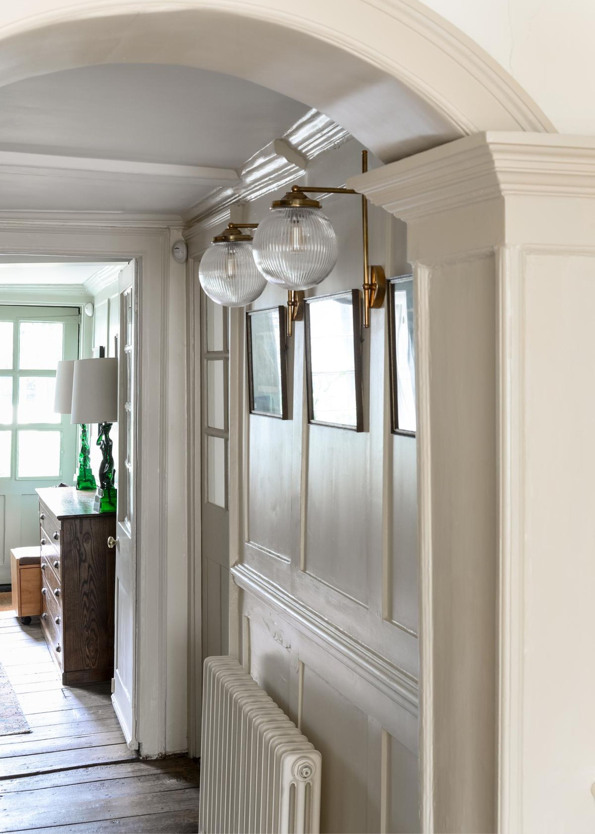 An entryway of a home with two lamps hanging near an arches ceiling and below the lights is a radiator