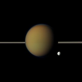 Saturn's moon Tethys, with its stark white icy surface, peeps out from behind the larger, hazy, colorful Titan in this Cassini view of the two moons. Saturn's rings lie between the two. NASA's Cassini spacecraft snapped this photo on May 21, 2011 and it w