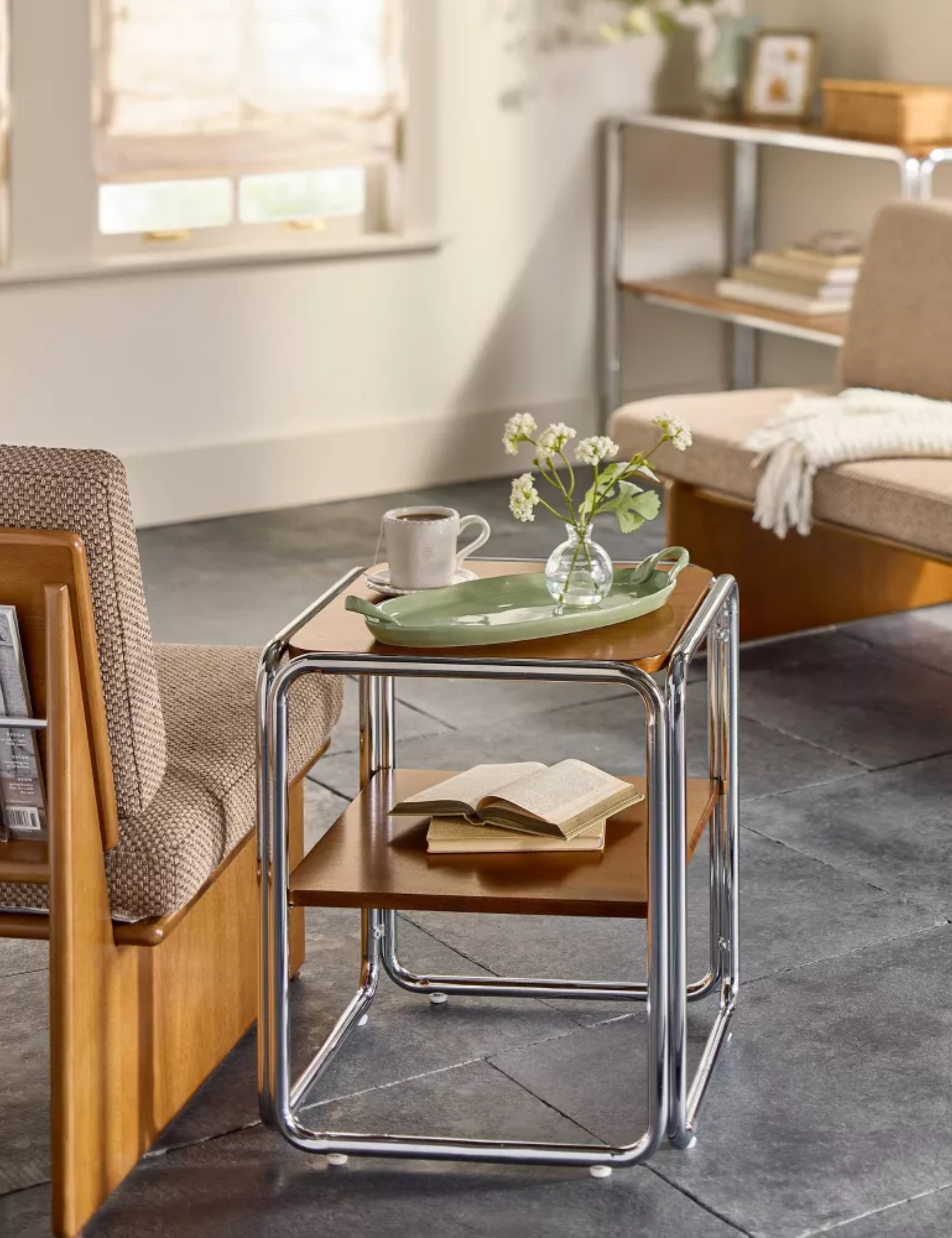 Mid-century style two-tier chrome and wood side table by Joanna Gaines pictured in a living room with slate tile floors and cream colored walls