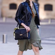 A passerby wears a black leather jacket, a flowing dress, a leather crossbody bag for travel, on May 19, 2020 in Paris, France.