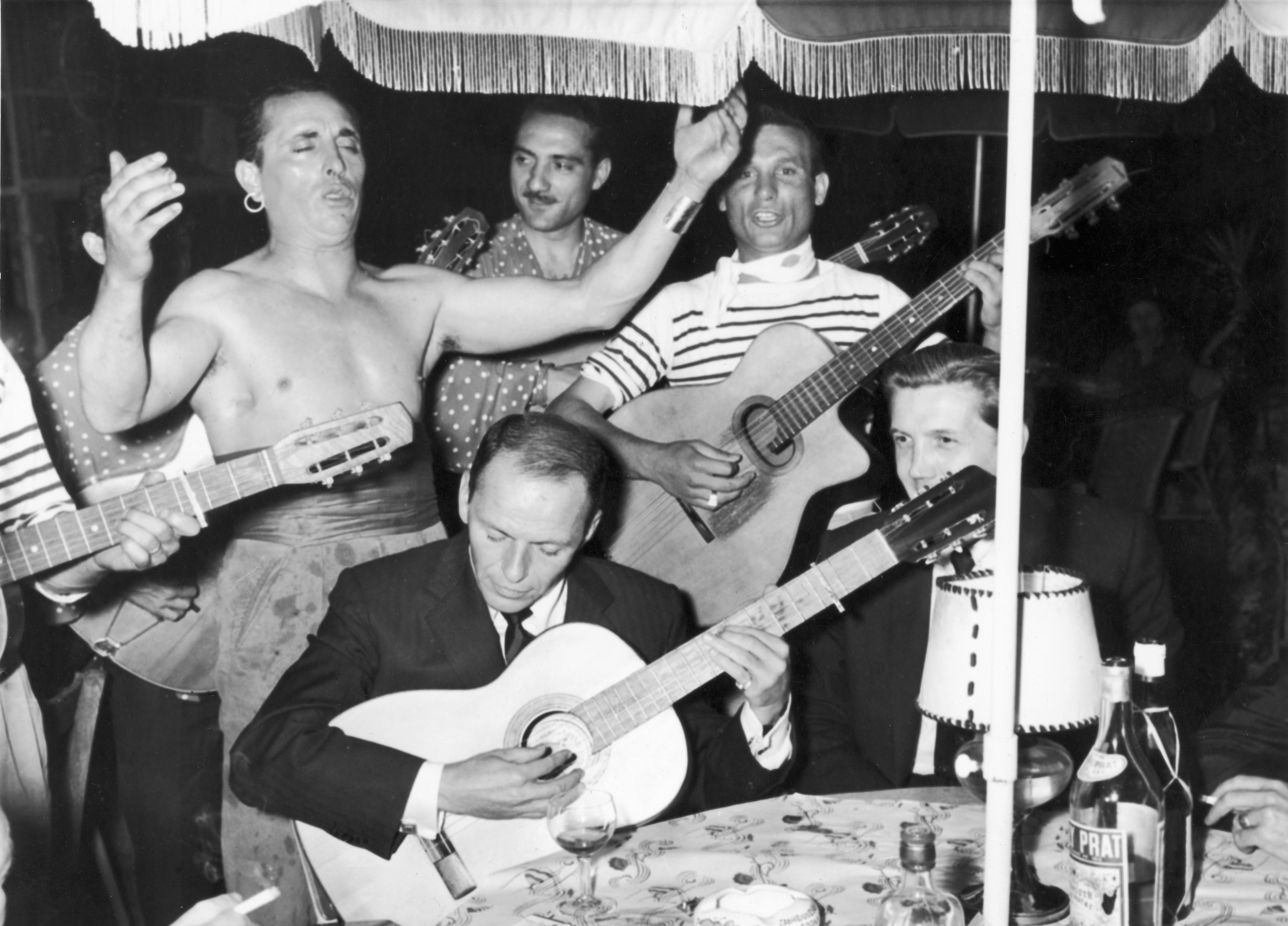 Frank Sinatra playing the guitar, surrounded by other people