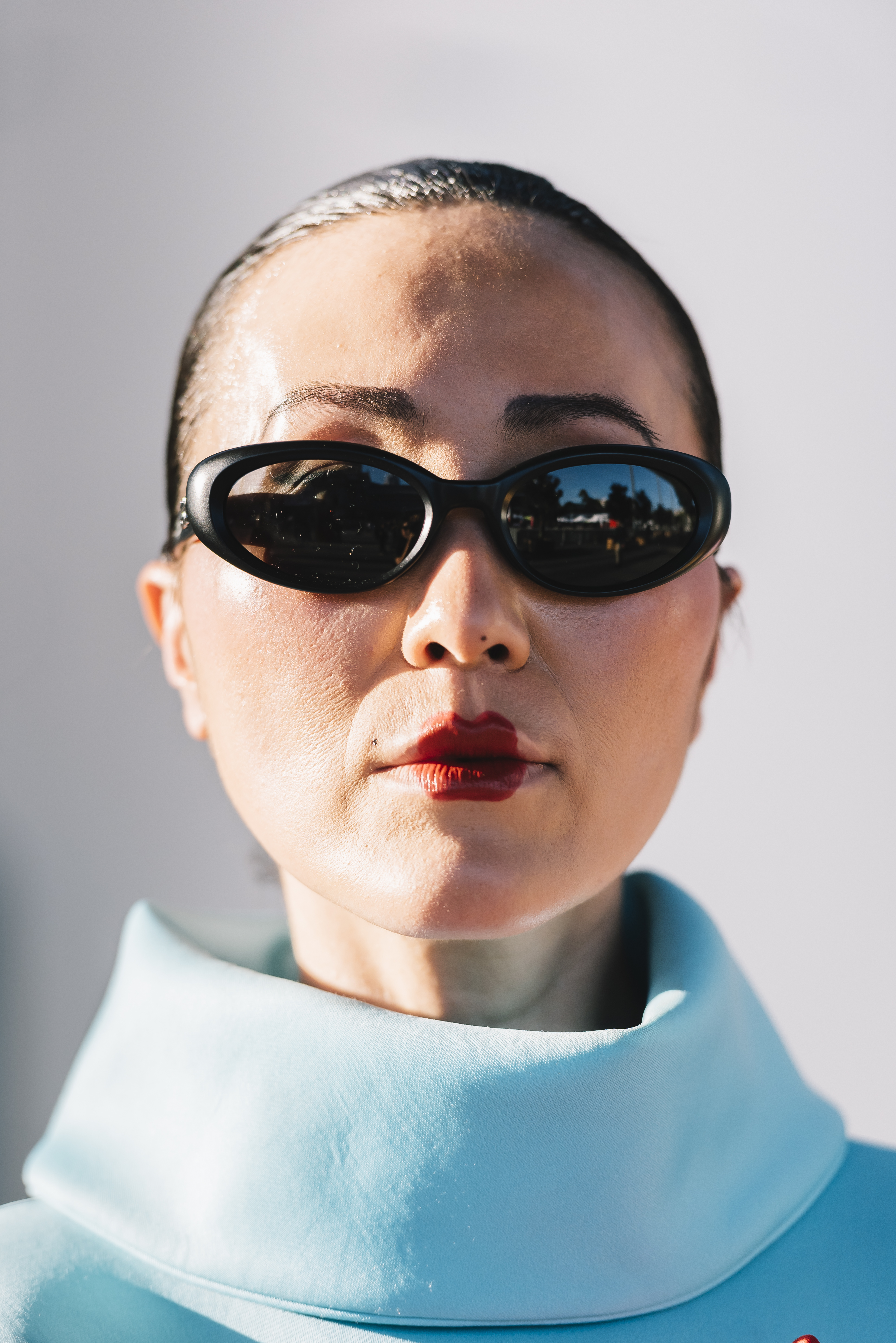 woman with thin eyebrows wearing heart-shaped red lipstick and black sunglasses with a light blue turtleneck
