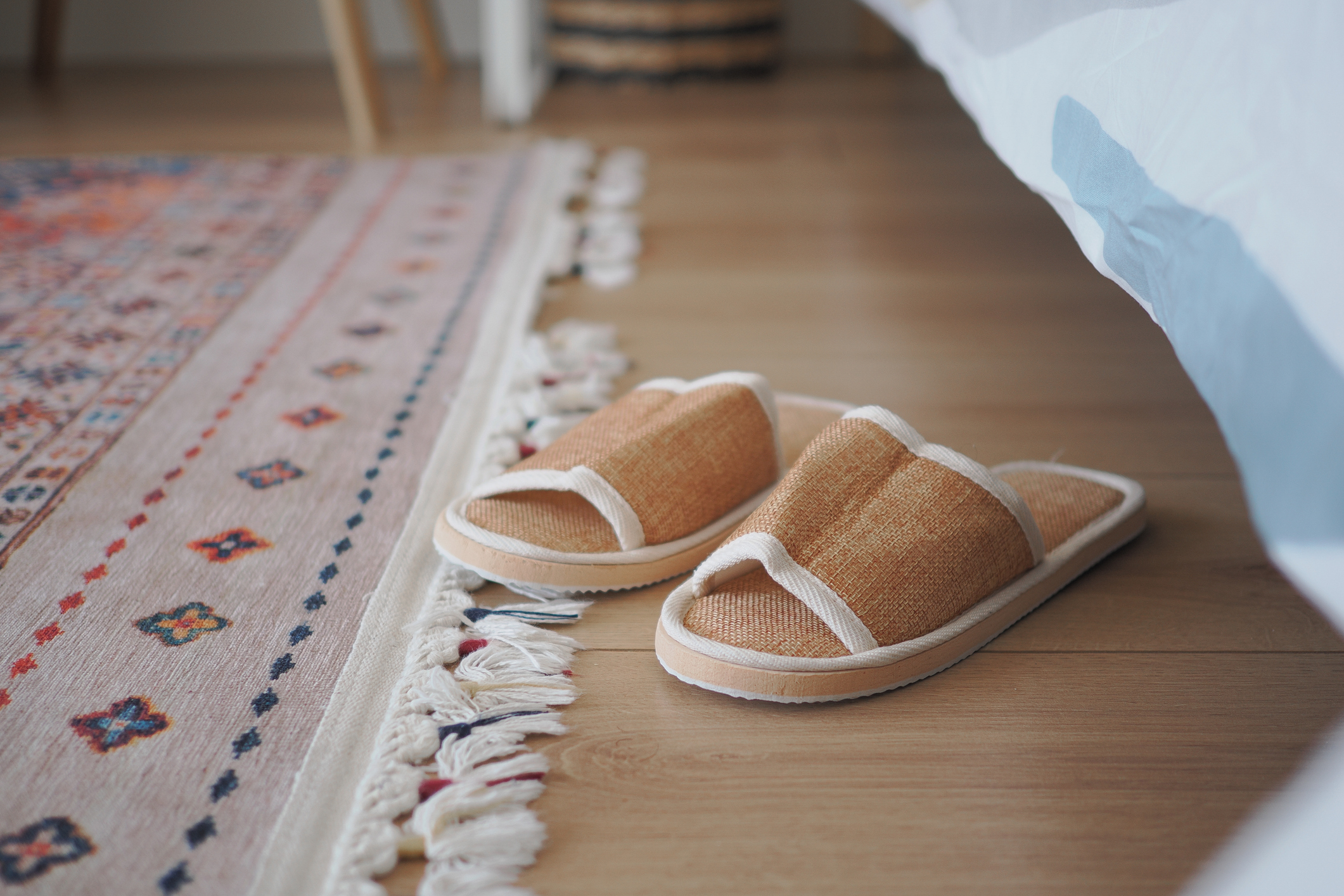 Slippers sit on the wood floor beside a colorful rug at home.
