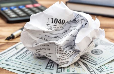 Crumpled tax form with money, calculator and notepad on the table. 