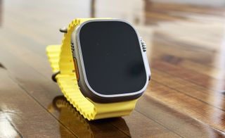 Apple Watch Ultra med gul rem på et trebord.