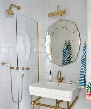 Scalloped wall mirror above sink in white bathroom, with brass fittings, and striped colored towels