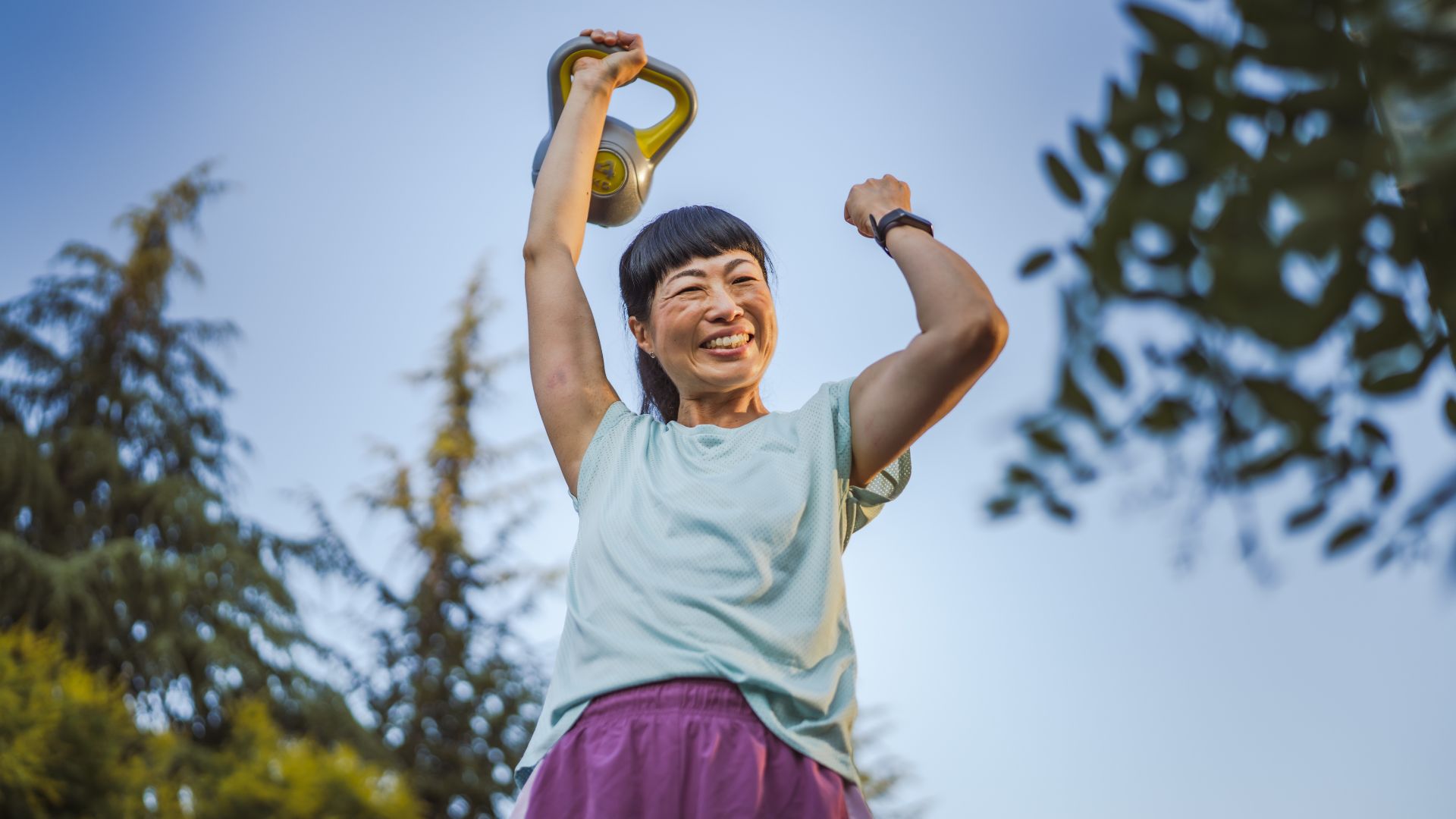 Woman doing 7-7-7 kettlebell workout, holding kettlebell above her head and smiling