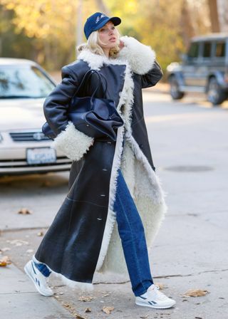 Elsa Hosk wearing a shearling coat, jeans, a baseball cap, The Row's Margaux bag, and a pair of Reebok Classic AZ sneakers.