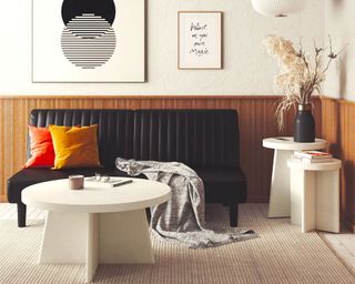 Living room with white round side tables and coffee table, black sofa, fluted paneling, natural rug