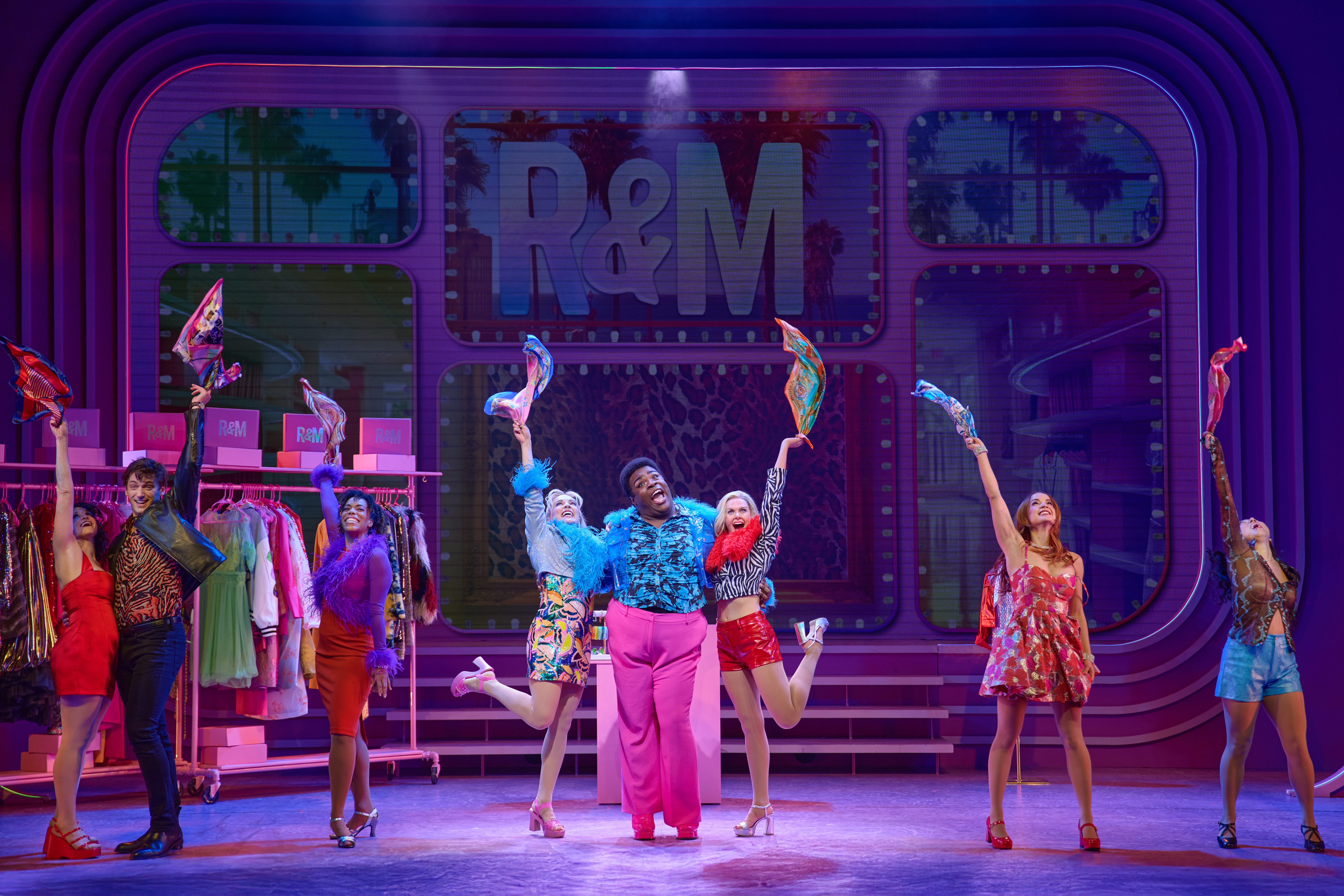 the company of romy and michele the musical dance on stage in colorful clothing and wave scarves in the air