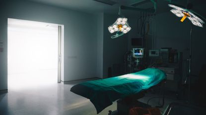 A hospital room with a bed and two lights hanging above it. The room is dark.