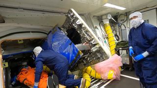NASA technicians load the "Moonikin" mannequin in an orange spacesuit through the Orion space capsule hatch.