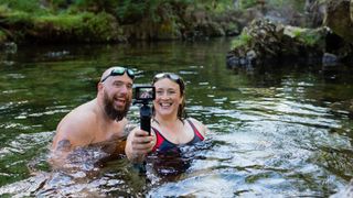 Couple laughing together open water swimming with camera, taking selfie