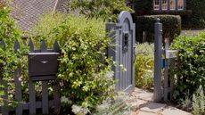 Mailbox landscaping ideas showing a gray mailbox on a gray picket fence with green bushes.