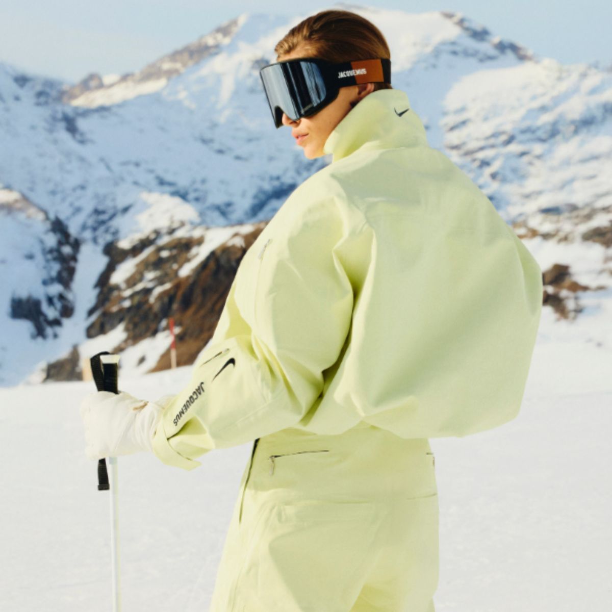 a model wears a yellow jacquemus + nike ski jacket on the slopes