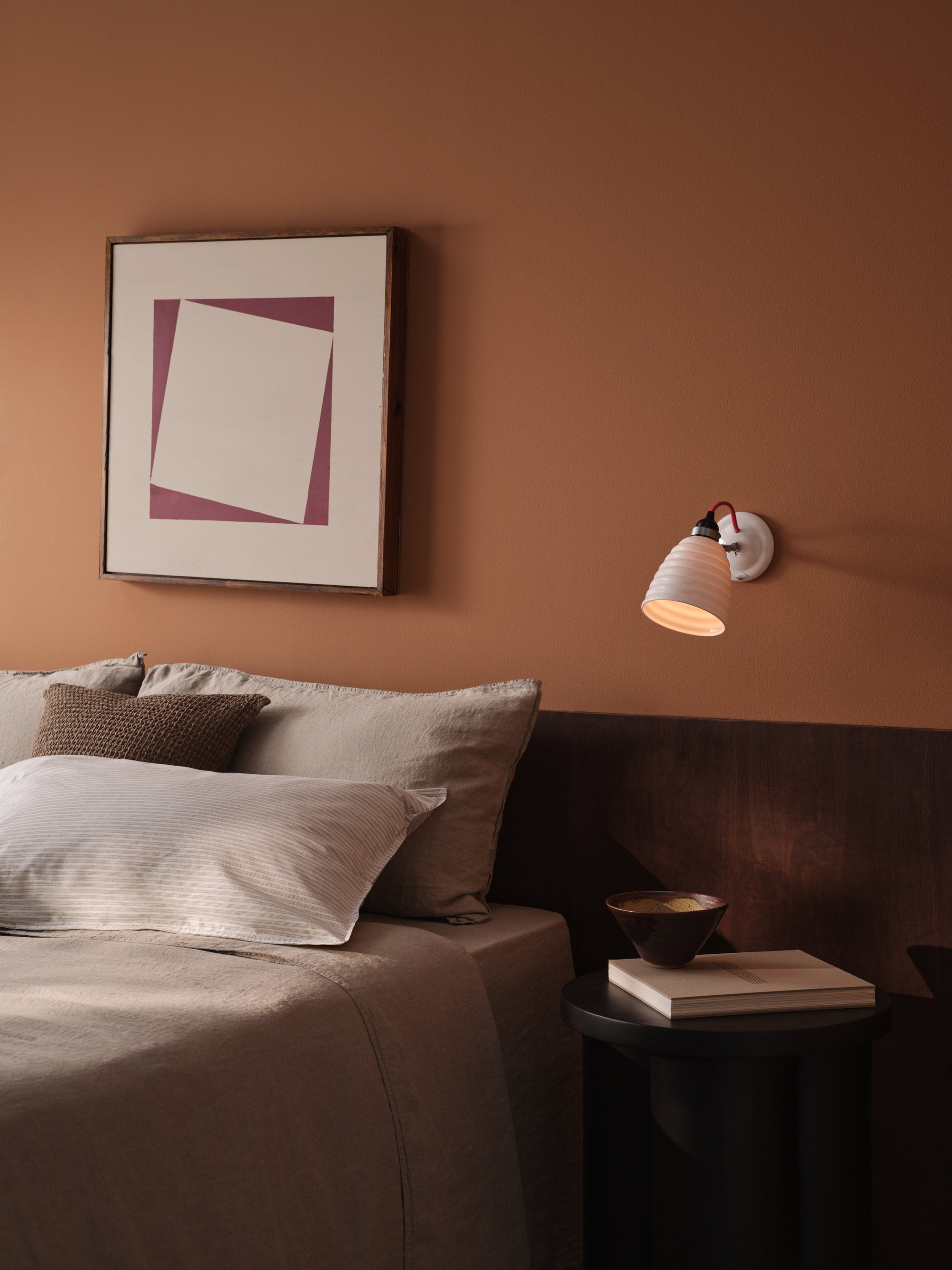brown bedroom with half-wall panel, artwork above bed, wall sconce, and timber bedside table