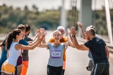 Happy senior woman greeting with her supporters while running a marathon on the road.