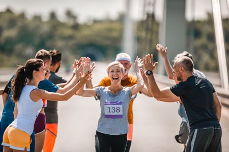 Happy senior woman greeting with her supporters while running a marathon on the road.