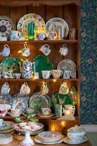 colorful china on a dresser with fairy lights and floral print wallpaper behind