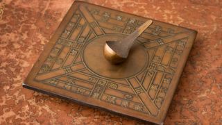 A reproduction of the world's first compass, a brown square object with a protrusion in the middle