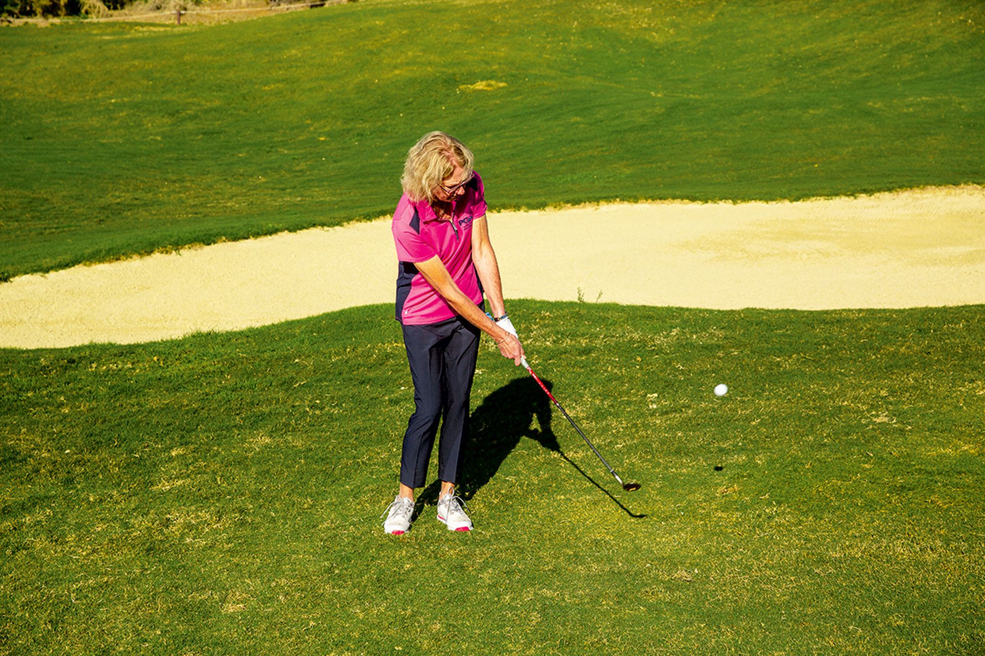 Sarah Bennett just past impact position with a wedge in her hand after hitting a chip shot towards a raised green