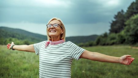 Smiling mature woman with arms outstretched in the countryside