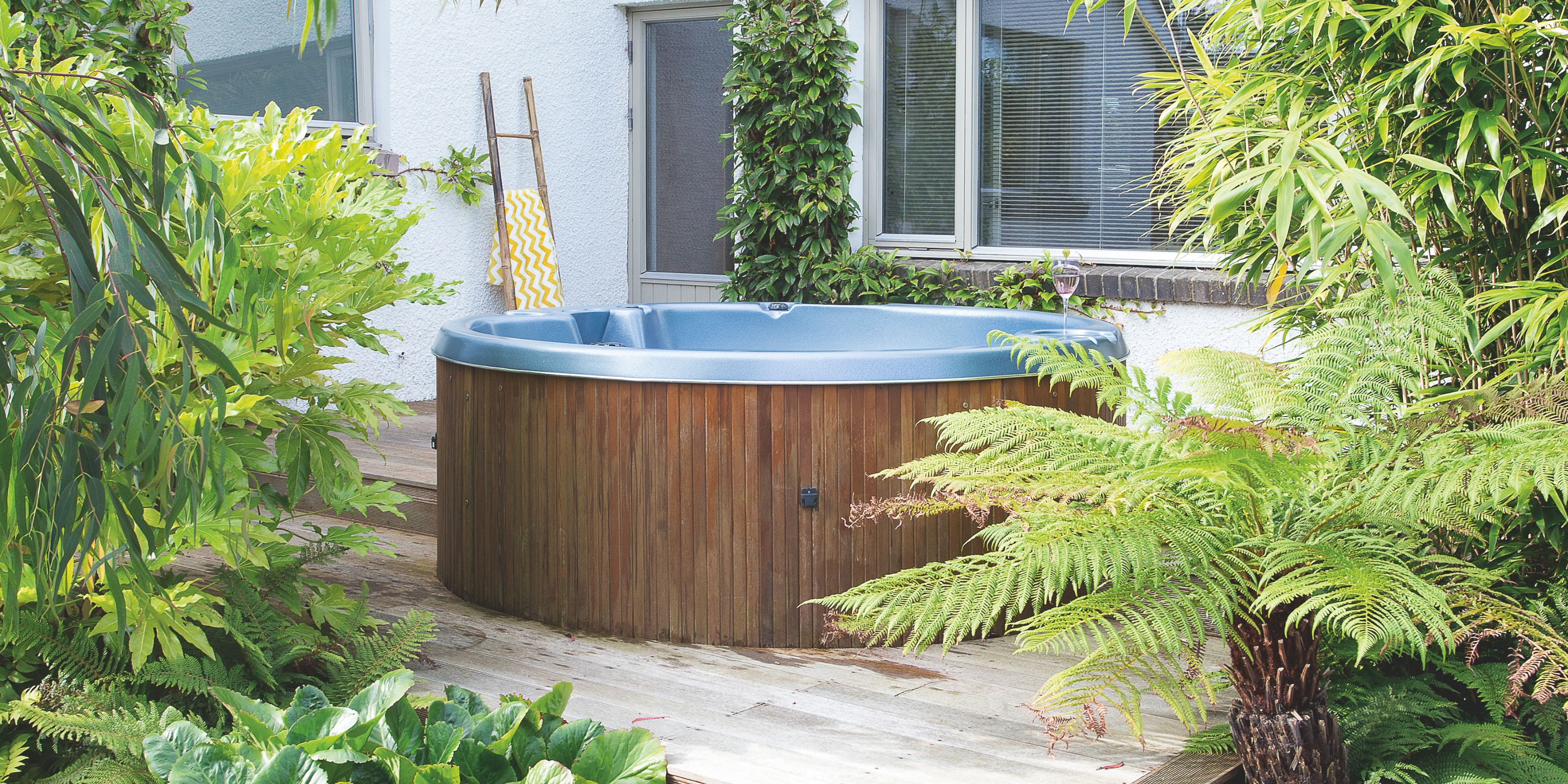 garden decking area with a hot tub framed by greenery