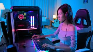 A woman sitting at a desk, using a gaming PC and LED keyboard