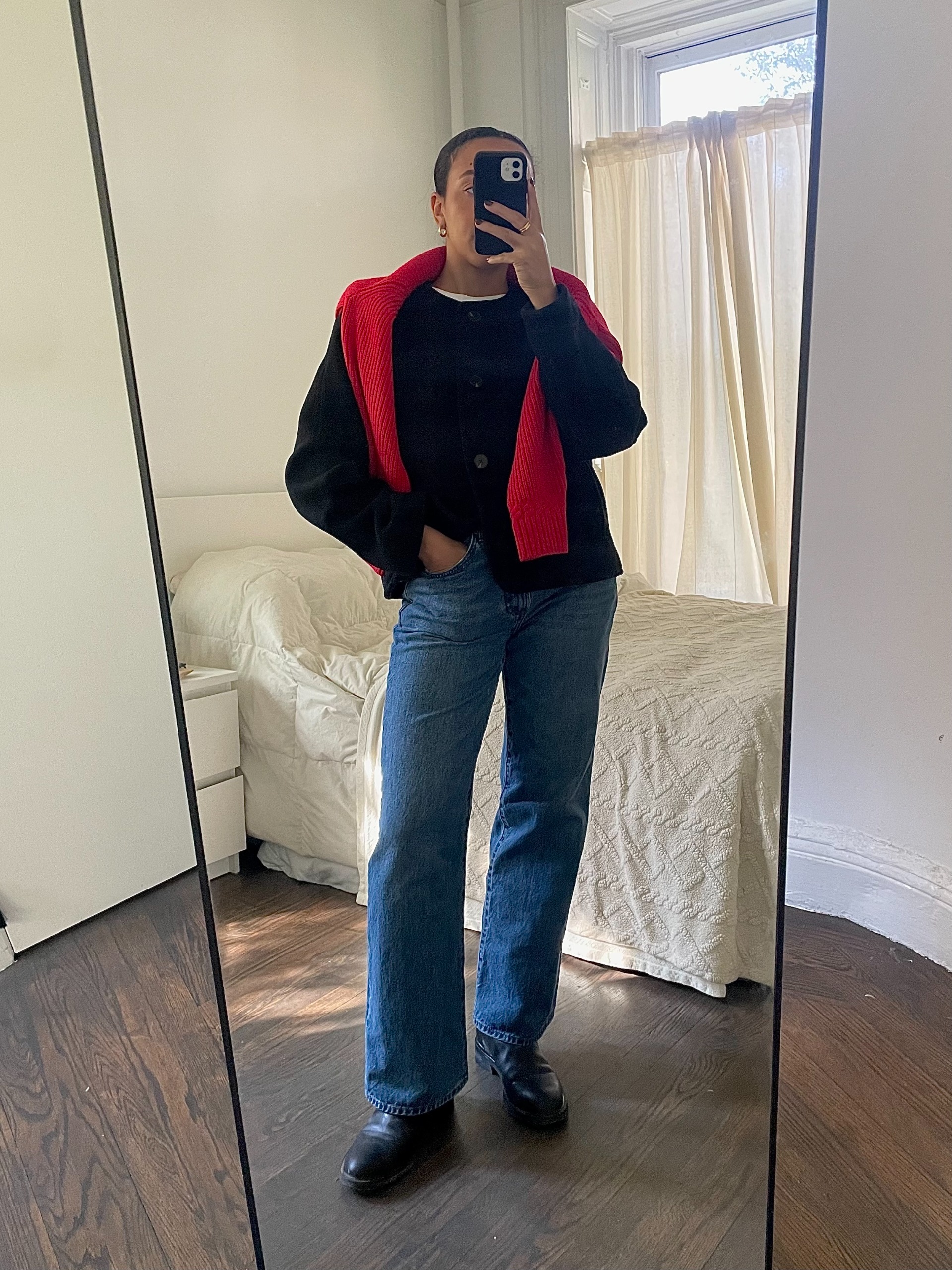 Lauren Tappan wearing a black coat, a red sweater, jeans, and black boots