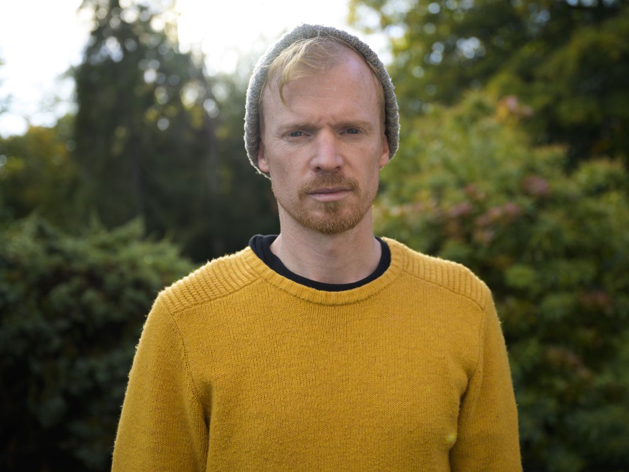 A man in a yellow jumper and hat standing in a garden
