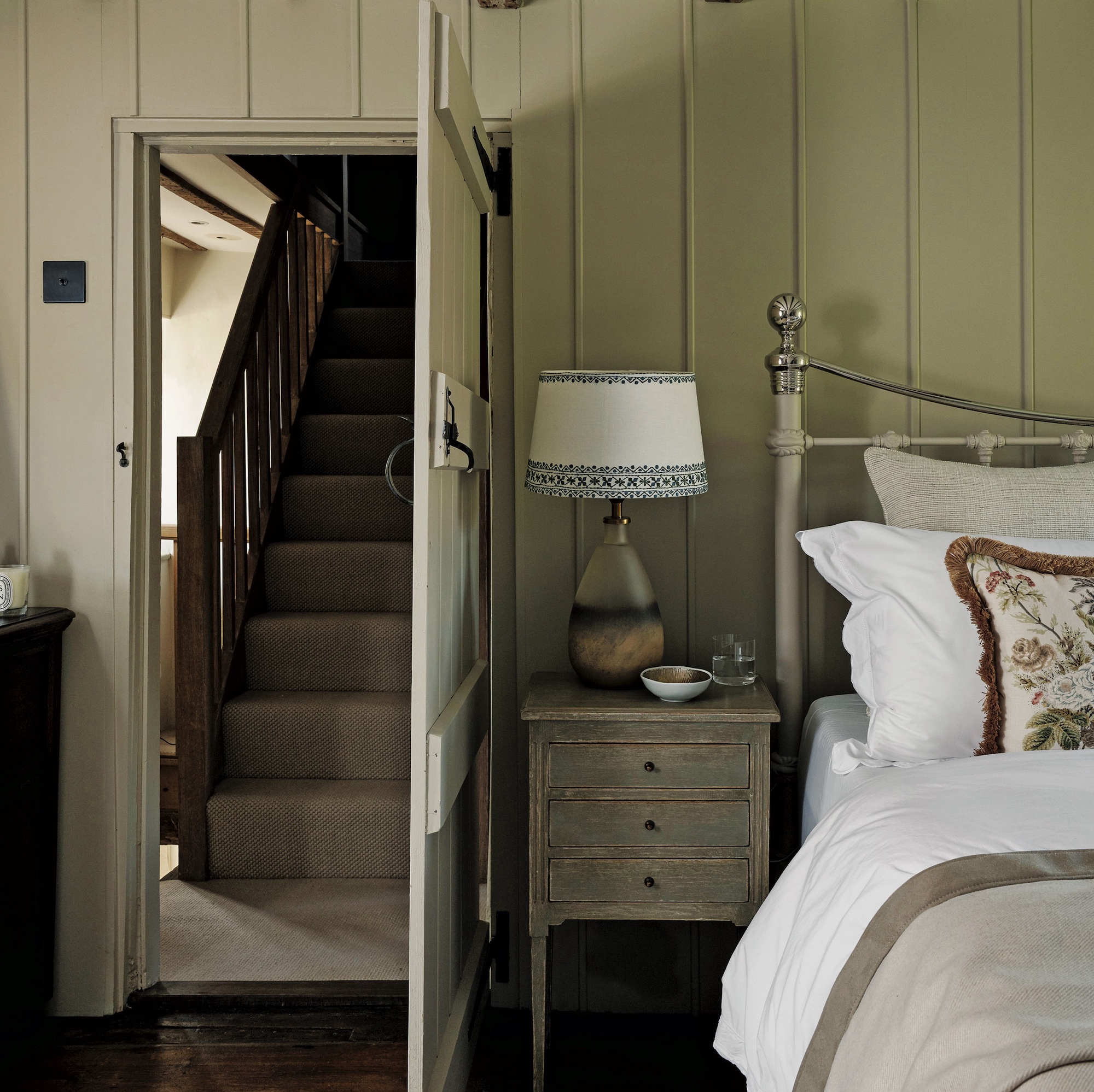 bedroom with wood panel wall, metal bedstead and wooden door leading to staircase