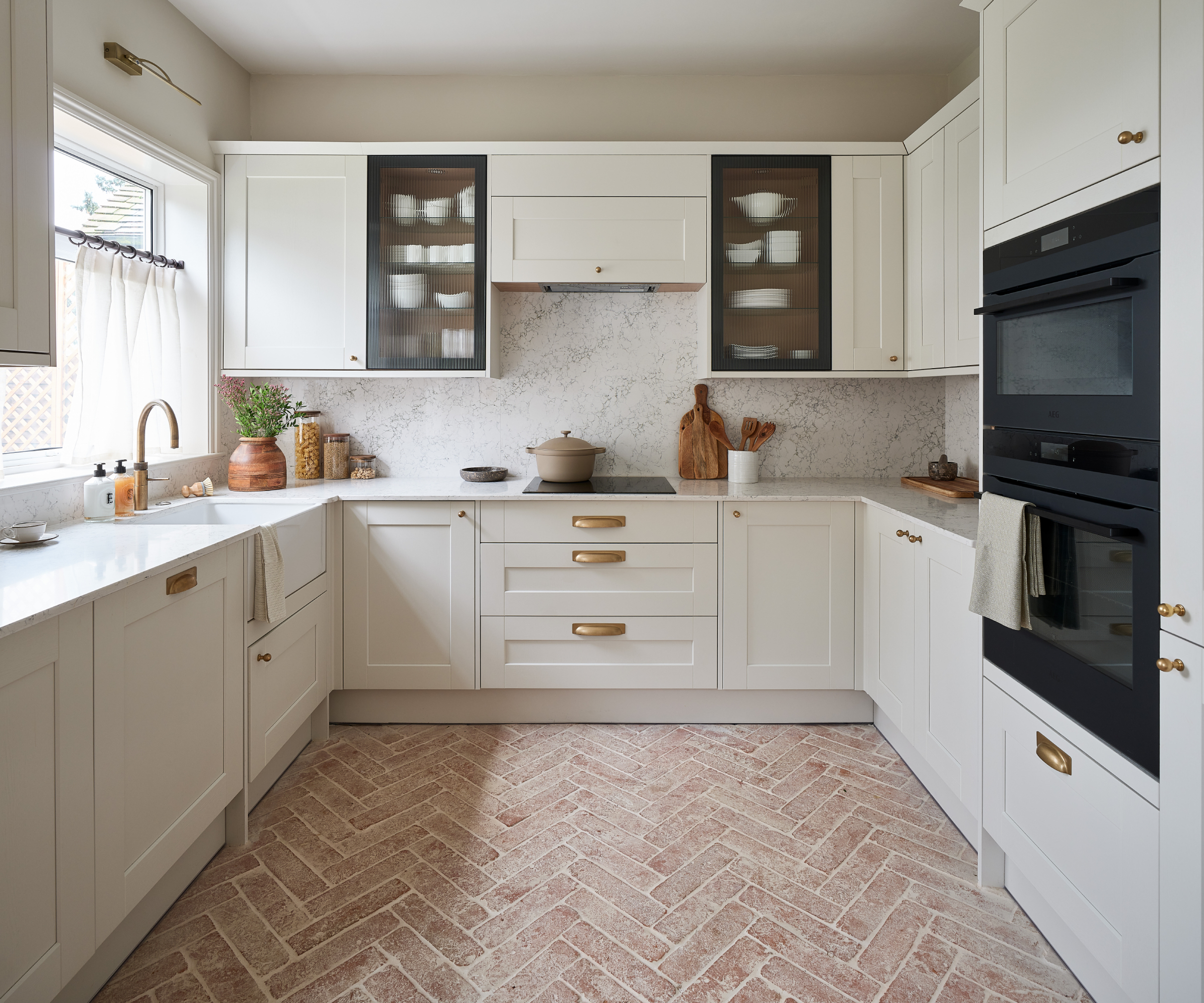 large white kitchen with brass hardware and light terracotta tiled floor in herringbone pattern