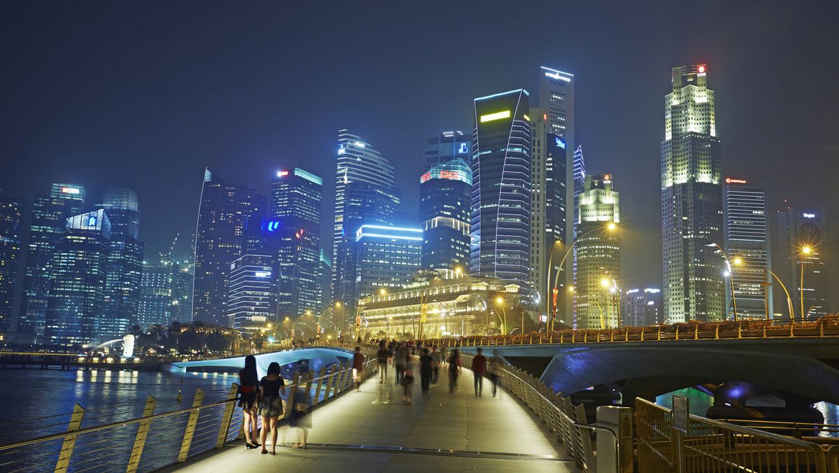 A long exposure photo of the Singapore skyline at night with people walking on a bridge in the foreground