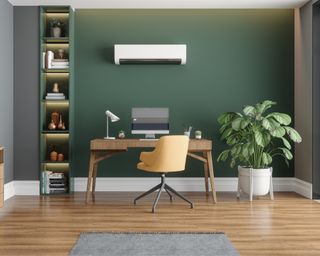Green small office with wooden desk and large floor planter