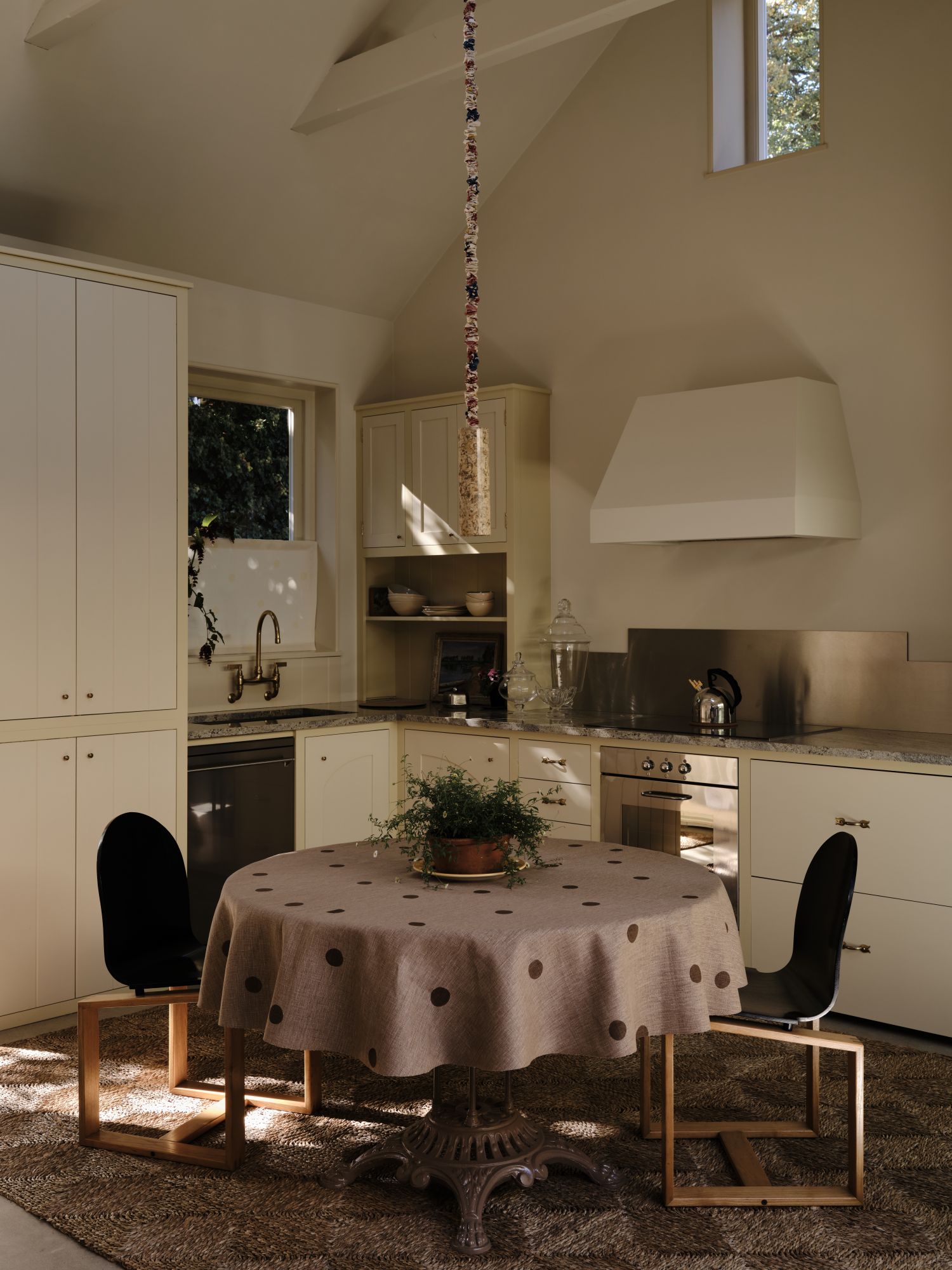 small corner kitchen with a dining table in the middle, cabinetry in off-white with a butter yellow trim surrounding them