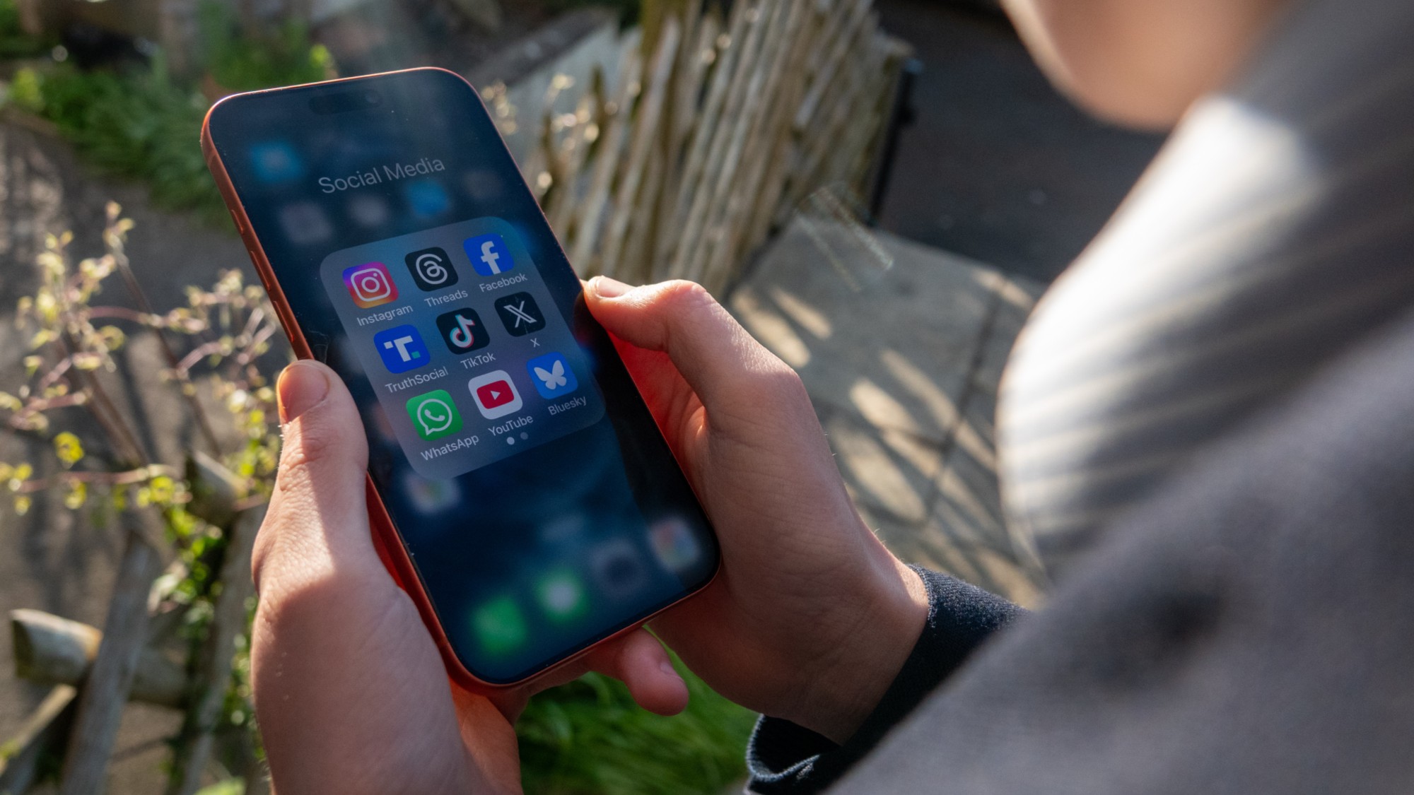 A 14-year-old boy holds a phone with various social media apps. 